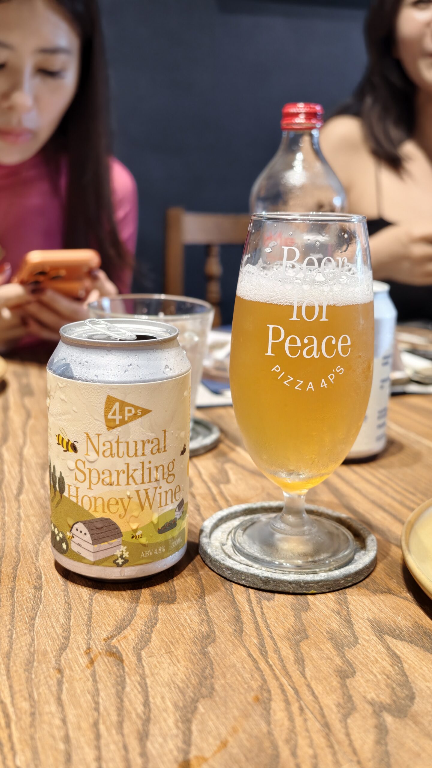  餐桌上放著一杯倒滿的 Pizza 4P's 自家品牌 Beer for Peace 精釀啤酒，旁邊還有一罐 Natural Sparkling Honey Wine 氣泡蜂蜜酒。